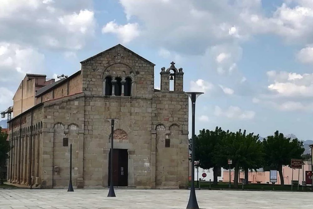sulla grande piazza la maestosa chiesa romanica di periodo medievale, con la sua facciata in granito e sulla destra il campanile a vela