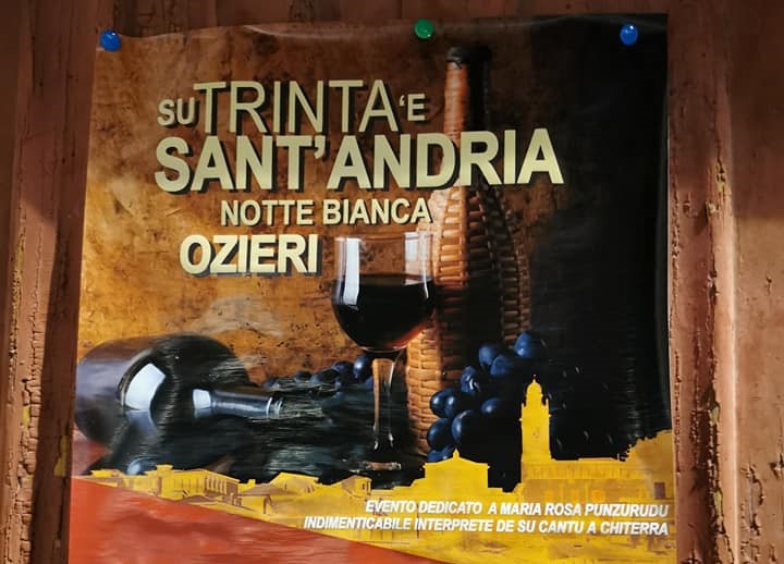 Locandina appesa su una porta in cui sono in primo piano un bicchiere di vino rosso, l'uva nera e una bottiglia leggermente dietro