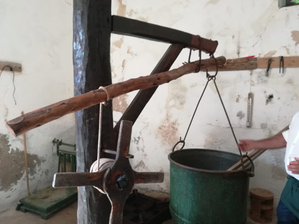 Un antico argano di legno con caldaia in rame appesa al gancio e una ruota che serviva per alzare e spostare la pesante caldaia