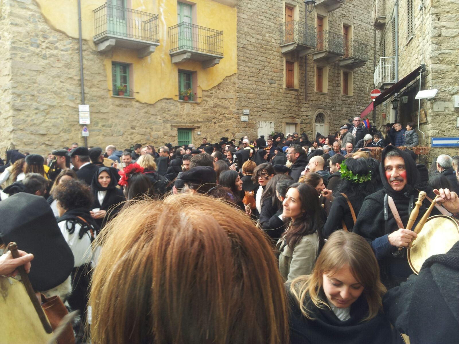 Carnevale Una folla di persone lungo le vie di un paese con le case di pietra e persone con cappotti di orbace di colore nero con cappuccio.