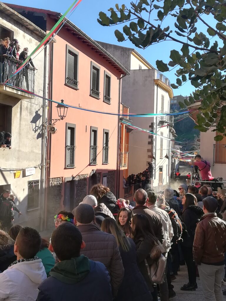 Tra le case e una folla di gente i cavalieri, che in foto non si vedono, arrivano a fine corsa. Si vede solo la polvere alzata dai cavalli.