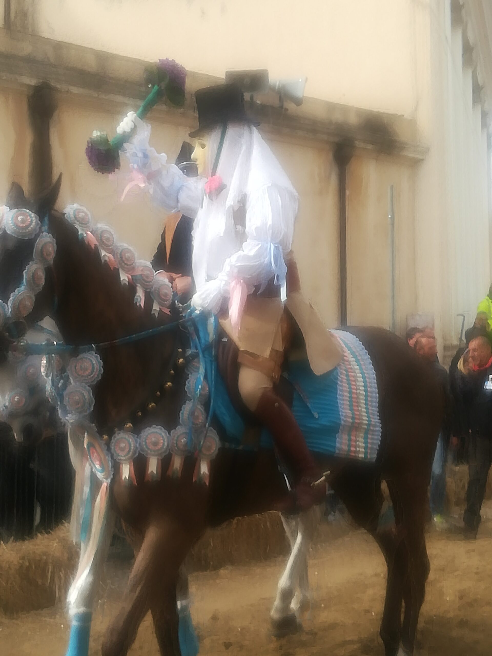 dig Su Componidori a cavallo. Immagine sfocata, il capo corsa è come avvolto nel suo alone di mistero: camicia bianca, maschera sensa nessuna espressione, alto cappello nero e immancabile il mazzo doppio di violette.