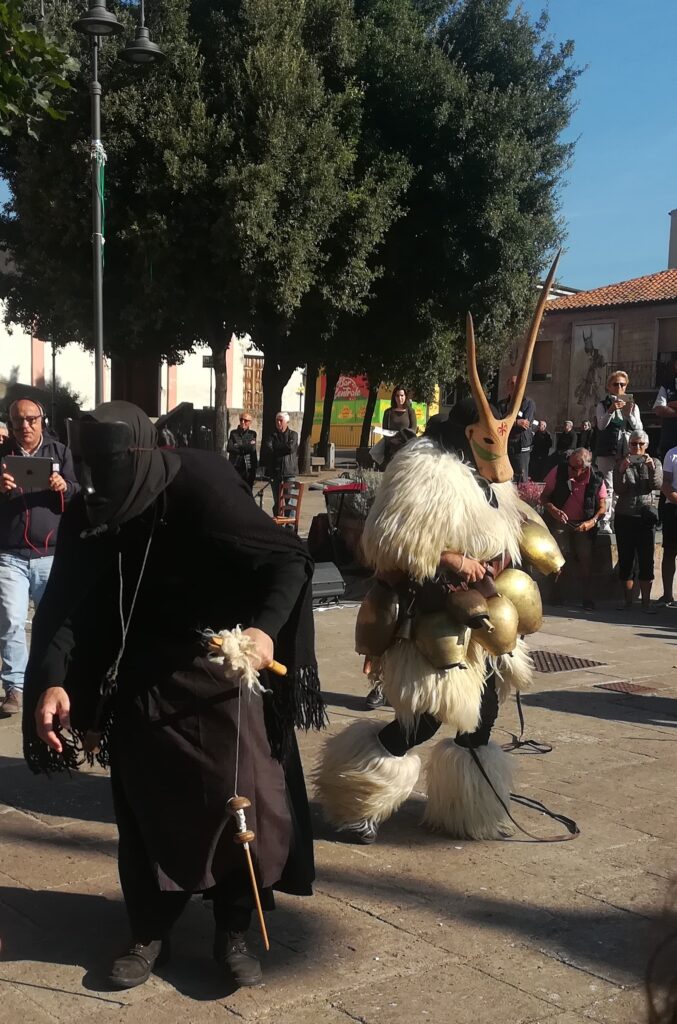 Lungo le vie del paese la sfilata. In primo piano la Filinzana tutta vestita di nero con il fuso, lo scialle, il fazzoletto e la maschera. Al suo fianco il Boe con i campanacci di bronzo come cinta, la pelle bianca e la maschera di legno con lunghe corna.